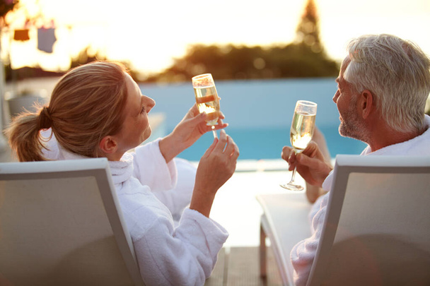 Σε μια ρομαντική απόδραση. Στιγμιότυπο ενός ώριμου ζευγαριού που πίνει σαμπάνια ενώ χαλαρώνει στις ξαπλώστρες το ηλιοβασίλεμα - Φωτογραφία, εικόνα