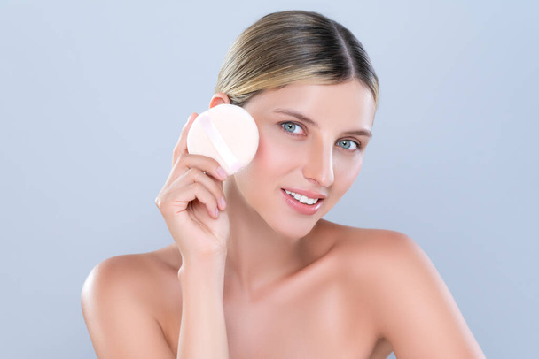 Alluring beautiful female model applying powder puff for facial makeup concept. Portrait of flawless perfect cosmetic skin woman put powder foundation on her face in isolated background. - Photo, Image