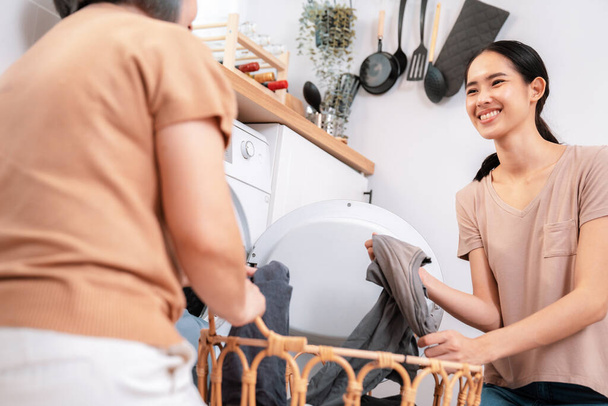 Daughter and mother working together to complete their household chores near the washing machine in a happy and contented manner. Mother and daughter doing the usual tasks in the house. - Photo, image