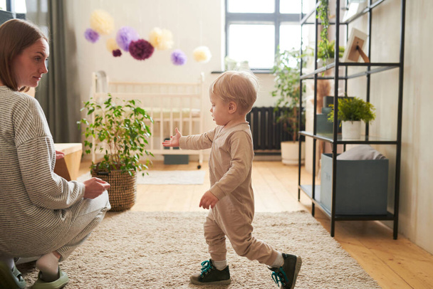 Kleine jongen reikt hand naar zijn moeder en vraagt haar om te helpen terwijl ze spelen in de kamer - Foto, afbeelding