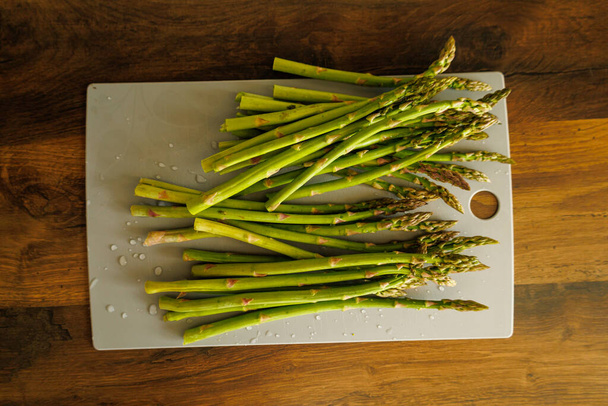 Fresh asparagus, just rinsed with drops of water, on a cutting board. - Фото, изображение