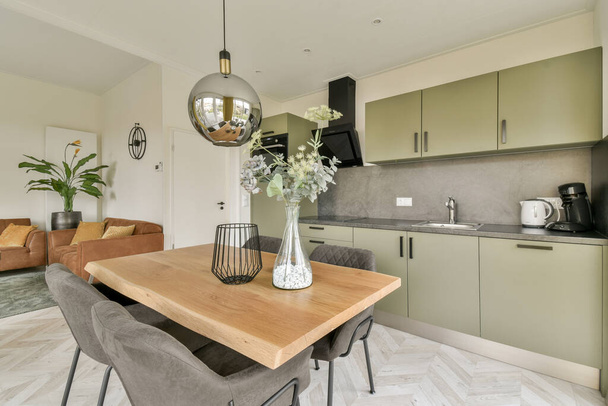 una cocina y comedor en una casa de estilo moderno con armarios de color verde claro, suelos de mármol blanco y mesa de madera - Foto, imagen