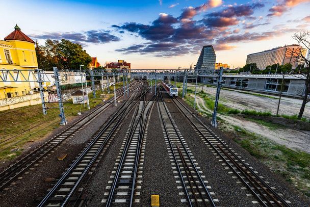Poznan, Polen - juli 2022: Het uitzicht vanaf de Teatralny brug op het spoor, rijdende treinen en de skyline van de stad bij zonsondergang - Foto, afbeelding