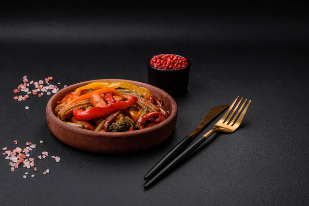 Μείγμα λαχανικών καλαμπόκι, καρότα, πιπεριές, μπρόκολο, κρεμμύδια σε σάλτσα teriyaki σε κεραμικό πιάτο σε σκούρο μπετόν φόντο - Φωτογραφία, εικόνα