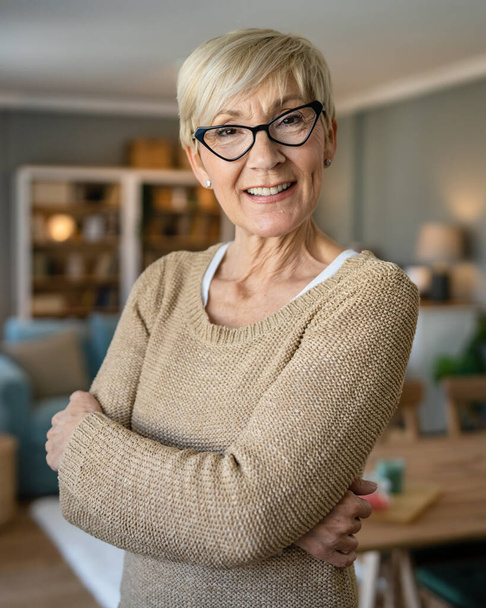 Κοντινό πλάνο πορτρέτο μιας ηλικιωμένης γυναίκας με κοντά μαλλιά χαρούμενο χαμόγελο θετική συγκίνηση αντίγραφο χώρο στέκεται στο σπίτι εσωτερική φορούν γυαλιά - Φωτογραφία, εικόνα