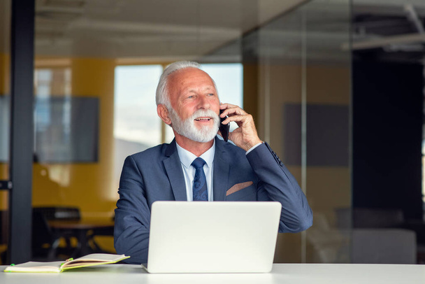 Przystojny, uśmiechnięty starszy mężczyzna siedzący w przytulnym miejscu pracy z laptopem w domu, emerytowany mężczyzna rozmawiający z przyjaciółmi w mediach społecznościowych - Zdjęcie, obraz