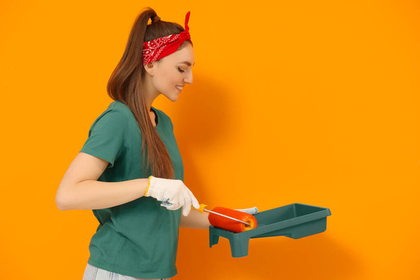 Happy designer with roller taking paint from container near orange wall - Photo, Image