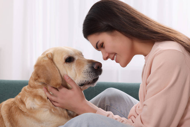 Happy woman with cute Labrador Retriever on sofa at home - Foto, afbeelding