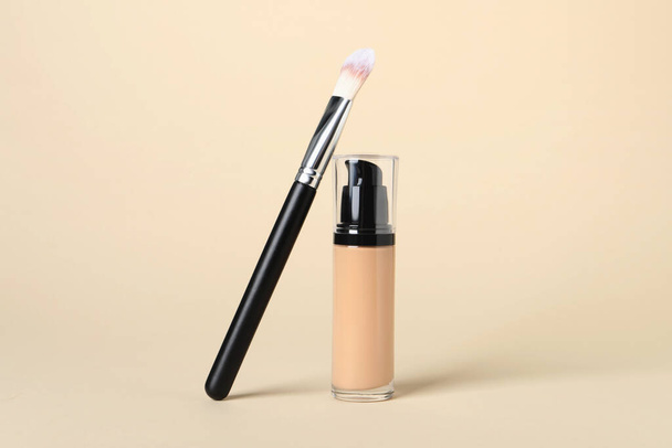 Bottle of skin foundation and brush on beige background. Makeup product - 写真・画像