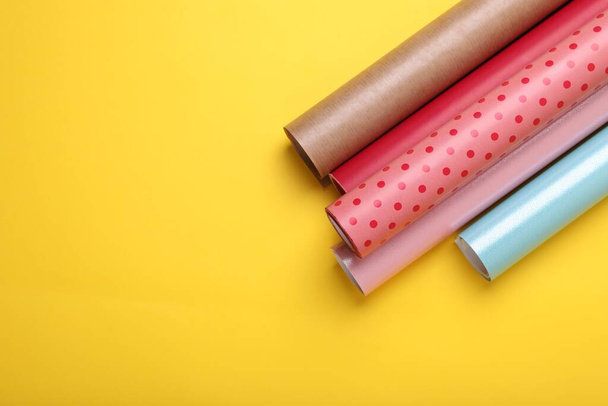 Rolls of colorful wrapping papers on yellow background, top view. Space for text - Фото, изображение