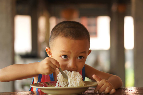 Le garçon utilise une cuillère pour déposer des nouilles alimentaires dans sa bouche pour manger. - Photo, image