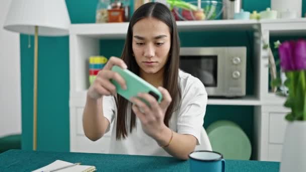 Молодая красивая латиноамериканка, играющая в видеоигры на смартфоне в столовой - Кадры, видео