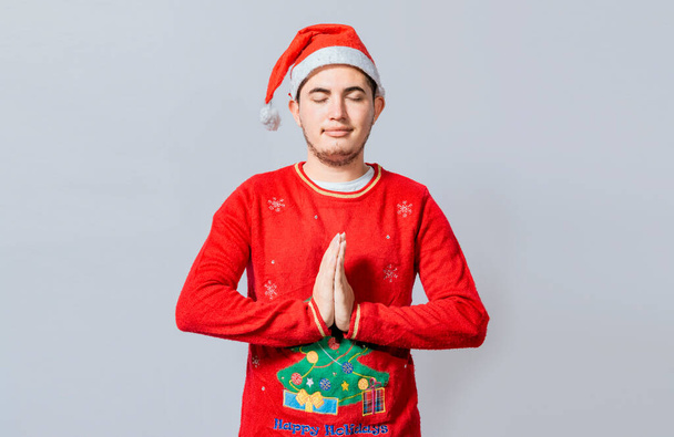 Guy with hands together praying in christmas isolated, concept of person with christmas hat praying and making a wish. Man with christmas hat with praying hands isolated - Photo, Image