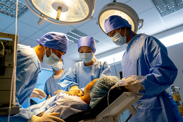 Ameliyathanedeki doktoru kapatın ve hastanedeki profesyonel ekip tarafından desteklenen hastayla ilgilenin.. - Fotoğraf, Görsel