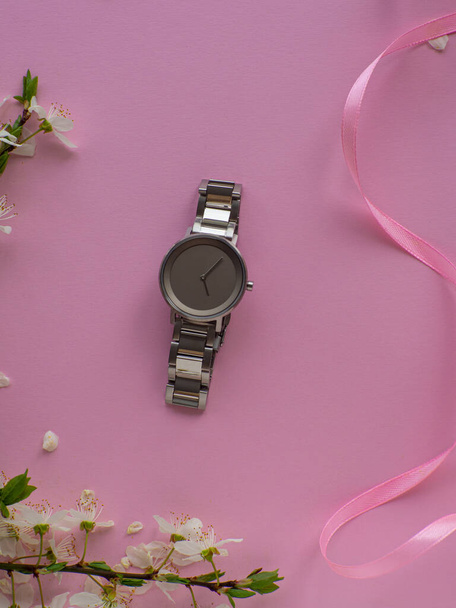 Womens hand watch on pink background with cherry flowers and copy space. Womens, Valentines and Mothers Day gift. Concept of beauty, elegance and femininity. Buying birthday gifts online. - Photo, Image