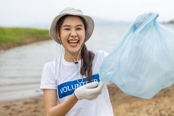 Щасливі азіатські жінки-добровольці, які тримають блакитні мішки для сміття, дивляться на камеру, заощаджуючи світ, зменшуючи глобальне потепління, волонтери чистять пластикові мішки відходами в природних пам'ятках
. - Фото, зображення