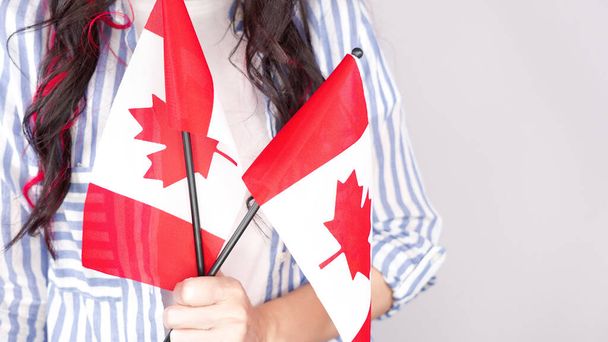 Unrecognized girl student in white blue shirt holding small canadian flag over gray background, Canada day, holiday, vote, immigration, tax, copy space. - Photo, Image