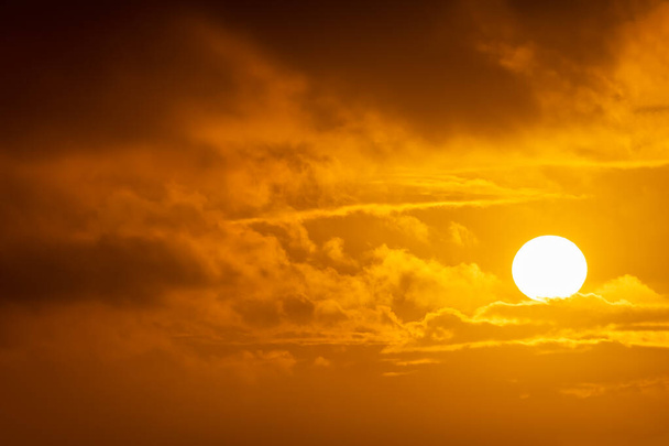 Gigantyczne słońce, które wydaje się zawieszone nad chmurami w złotym i spektakularnym zachodzie słońca - Zdjęcie, obraz