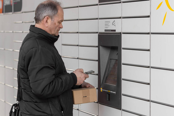 Pniewy, Polonya - 22 Mart 2023. Akıllı telefonu olan kıdemli bir adam posta servisindeki alışveriş dolabını açmak için şifre giriyor ya da kutu gönderiyor. E-ticaret nakliye ve teslimat konsepti. - Fotoğraf, Görsel