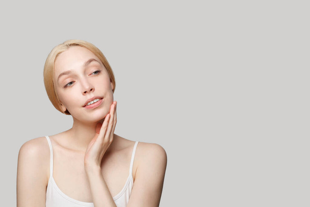 Hübsche Model-Frau, die beiseite schaut auf grauem Studiowand-Banner Hintergrund mit Kopierraum. Gesichtsbehandlung, Hautpflege und Kosmetologie-Konzept - Foto, Bild