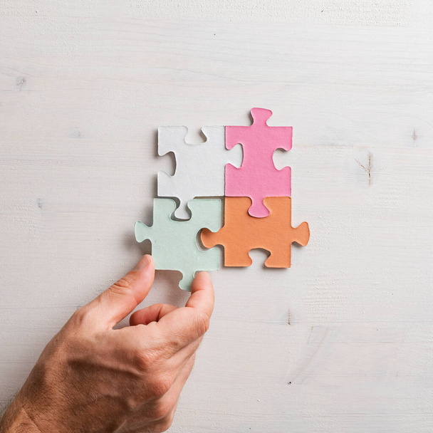 Top view of male hand joining four matching colorful puzzle pieces over wooden background Conceptual of solution, merger and implementation.  - Photo, Image