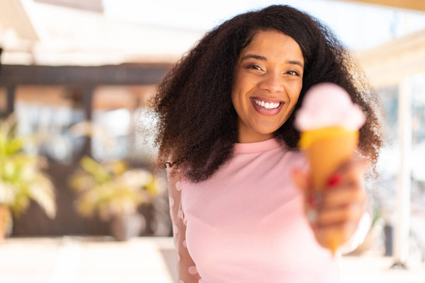 屋外でコーンアイスクリームを持つ若いアフリカ系アメリカ人女性 - 写真・画像