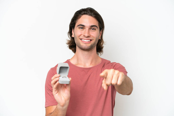 Young handsome man holding a engagement ring isolated on white background points finger at you with a confident expression - Photo, Image