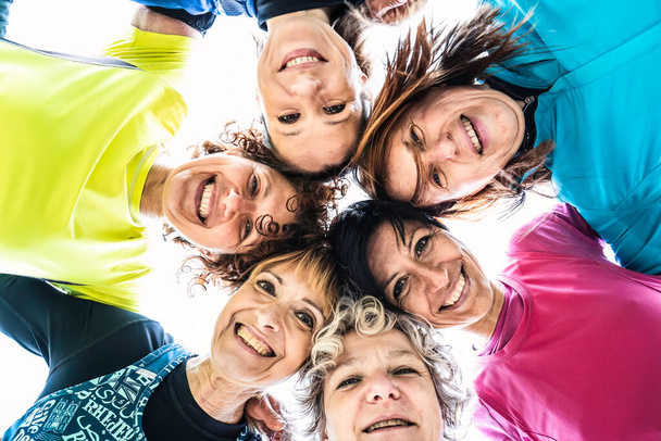 Мультипоколения подруги обнимаются в кругу и смотрят вниз на камеру после спортивных тренировок на открытом воздухе - Счастливые женщины нескольких поколений, веселящиеся вместе в городском парке - Яркий фильтр - Фото, изображение