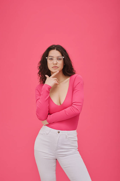 Ritratto di giovane donna sicura di sé in occhiali in posa davanti alla macchina fotografica su sfondo rosa - Foto, immagini