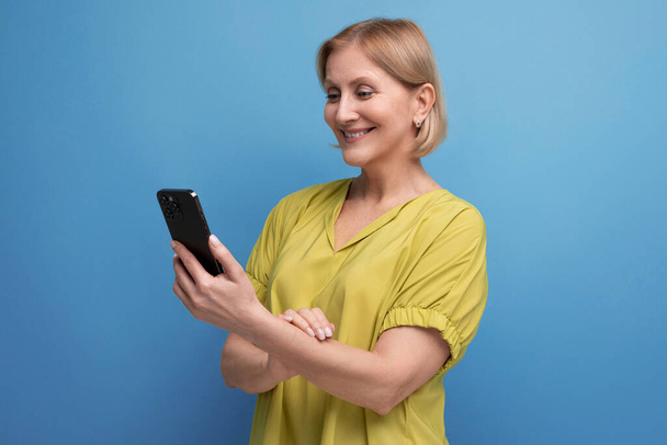 przyjemny blondynka w średnim wieku kobieta trzyma gadżet telefon w jej rękach pionowo. - Zdjęcie, obraz