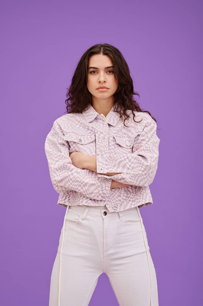 Retrato de mujer joven de confianza en sí misma de pie en ropa blanca con los brazos cruzados contra el fondo púrpura - Foto, Imagen