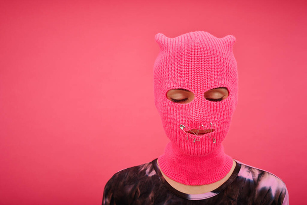 Portrait of yung girl in pink balaclava with closed mouth and eyes having no rights isolated on p - Фото, изображение