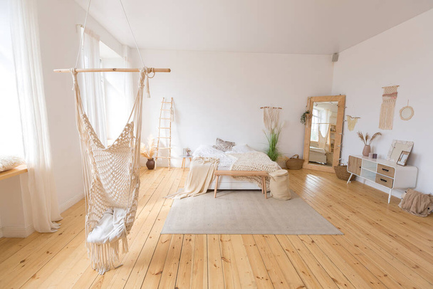 cute cozy light interior design of the apartment with a free layout of the kitchen and bedroom areas. a lot of windows, a wooden floor and a hanging swing. - Fotó, kép