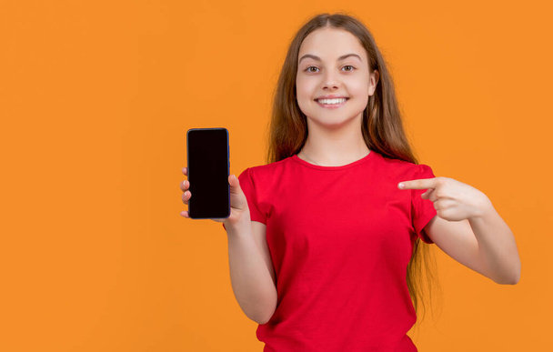 happy child pointing finger on smartphone on yellow background. - Photo, image