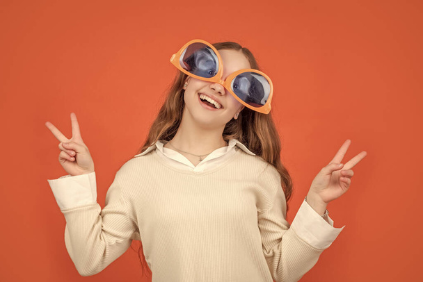 Happy girl wearing big funny sunglasses upside-down making V-sings gesture brown background, victory. - Fotó, kép