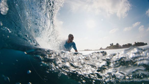 Surfer rides the wave. Young man surfs the ocean wave in the Maldives, splitted above and underwater view - Fotografie, Obrázek