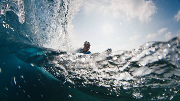 Surfer rides the wave. Young man surfs the ocean wave in the Maldives, splitted above and underwater view - Foto, afbeelding