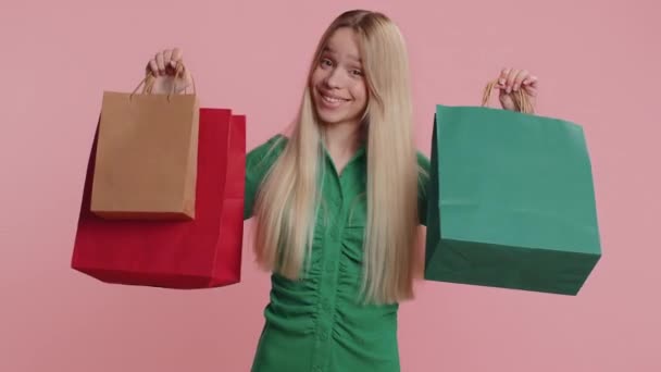 Zakupowa kobieta pokazująca torby na zakupy, rabaty reklamowe, uśmiechnięta wyglądająca na zdumioną niskimi cenami, robiąca zakupy w święta Black Friday. Młoda dziewczyna świętować zwycięstwo odizolowane na różowym tle studio - Materiał filmowy, wideo