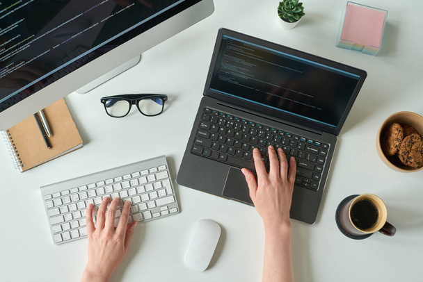 Wysoki kąt widzenia młody programista pisanie kodu na laptopie i za pomocą klawiatury komputerowej przy stole - Zdjęcie, obraz