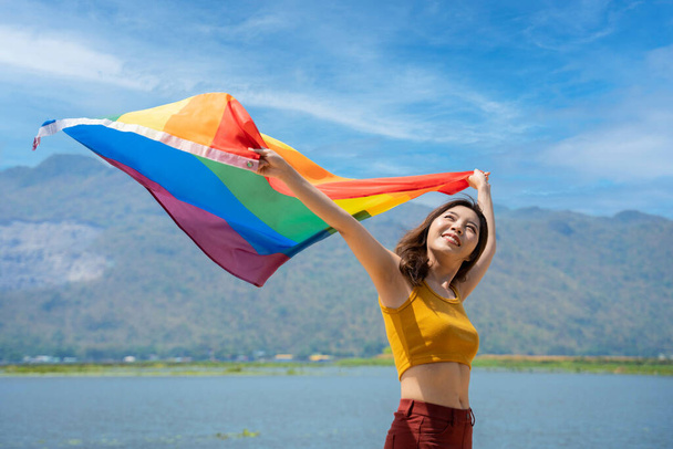 Lesbian woman with gay pride, rainbow flag on the beach against the sky. young woman smiling and raising and waving the LGBT flag in the air on the beach. - Foto, Bild