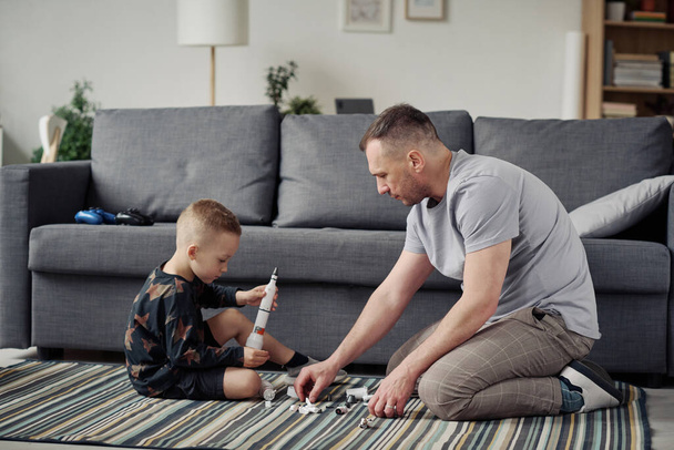 Nuori isä kerää rakentaja poikansa lattialla olohuoneessa - Valokuva, kuva