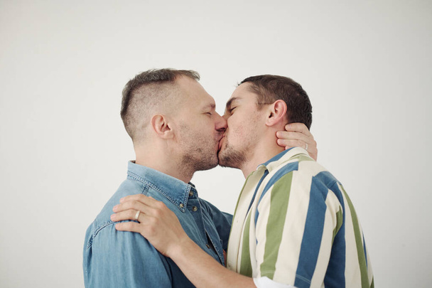 Portrait of two young men kissing each other against white background - 写真・画像
