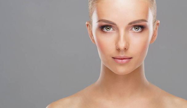 Beautiful face of young and healthy girl over grey background. Skin care, cosmetics and face lifting concept. - 写真・画像