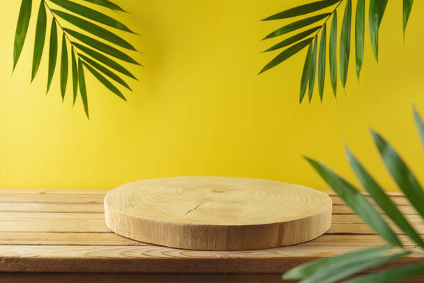 Empty wooden log with palm tree leaves on wooden table over yellow background . Summer mock up for design and product display - Photo, image