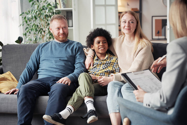 Mladí rodiče s adoptivním dítětem sedí na pohovce a mluví se sociálním pracovníkem během jejich setkání doma - Fotografie, Obrázek