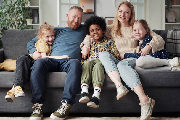 Nagy örökbefogadó család portréja, gyermekekkel a kanapén, ölelkezve és mosolyogva a kamerába. - Fotó, kép