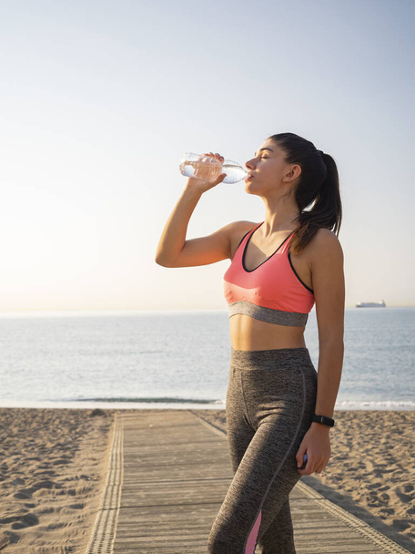 молодая женщина пьет воду из бутылки на пляже - Фото, изображение