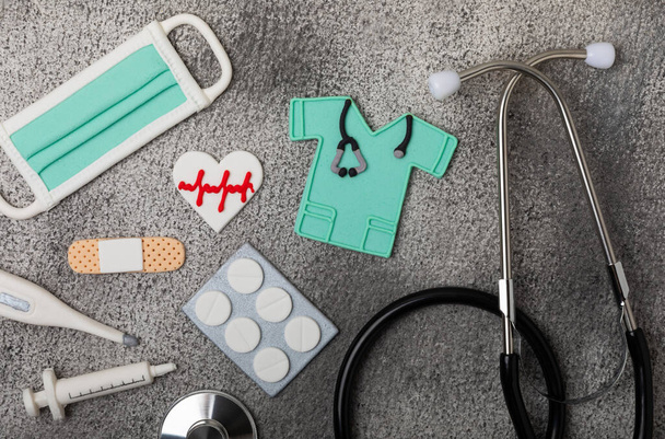 National Day of Doctors. Modern stethoscope, gift box and gingerbread in the form of medical supplies on a marble background. .Gingerbread in the form of a thermometer, a medical mask, a pill, a patch. - Foto, imagen