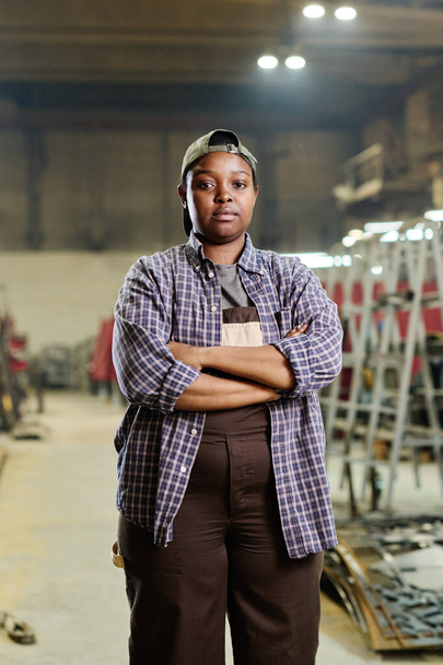 Portret afrykańskiej pracowniczki stojącej w zakładzie z skrzyżowanymi rękami i patrzącej w kamerę - Zdjęcie, obraz