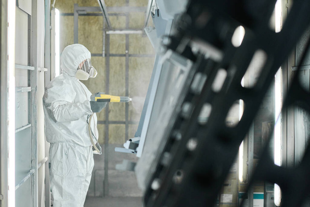 Teollisuuden työntekijä suojaava työvaatteet käyttäen ruiskupistooli maalata metalli yksityiskohtia tehtaalla - Valokuva, kuva
